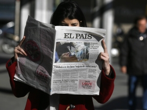 A woman poses with a first edition copy of Spanish newspaper El Pais in central Madrid...A woman poses with a copy of the January 24 first edition of Spanish newspaper El Pais in central Madrid January 24, 2013. Spain's influential El Pais newspaper withdrew what it said was "false photo of Hugo Chavez" that it had published in its on-line and print editions on Thursday. The grainy photo that El Pais originally splashed on its front page, billed as a global exclusive, portrayed the head of a man lying down with a breathing tube in his mouth. REUTERS/Andrea Comas  (SPAIN - Tags: MEDIA POLITICS)